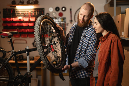 Two person examine bicycle wheel in repair workshop. Woman Assisting her husband Professional...