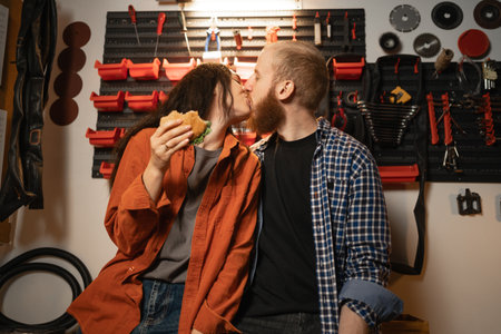 Kissing couple in garage, man and woman eating burgers and kissing after renovation in workshop.の写真素材