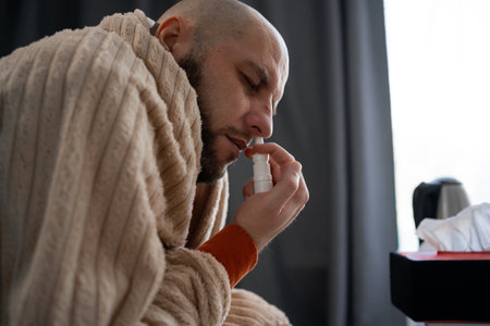 A sick man suffering from a cold uses a nasal spray for a runny nose. Flu treatment conceptの写真素材