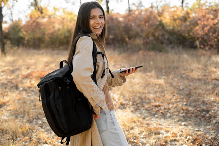 Photo of hispanic woman write sms carry bag wear fall style clothing walking in park outdoors