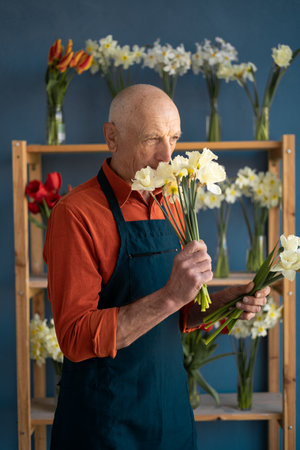 European elderly man florist inhales the smell of flowers.の写真素材