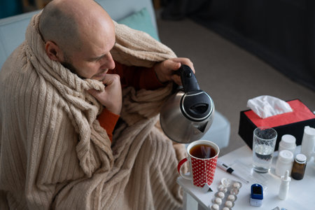Top view of a man making tea sick at home suffering from high fever and headache. Medicine and...