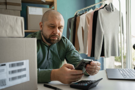 salesperson in store holds phone in his hands and prints an SMS to the client about the readiness of the parcel. Small business.の写真素材