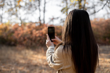 Woman taking nature photo on smartphone photographing an autumn forest on mobile phone camera. Tourism and hobbyの写真素材