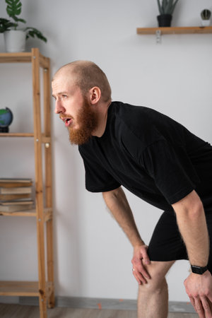 Sweating bearded man tired after a cardio workout for fitness. exhausted and sweating male athlete or runner resting after exercise at homeの写真素材