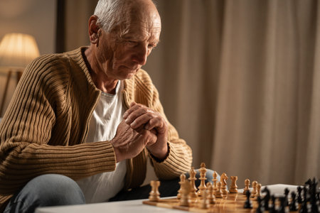 Thoughtful elderly man playing Chess on chess-board game at home for training brain memory and...