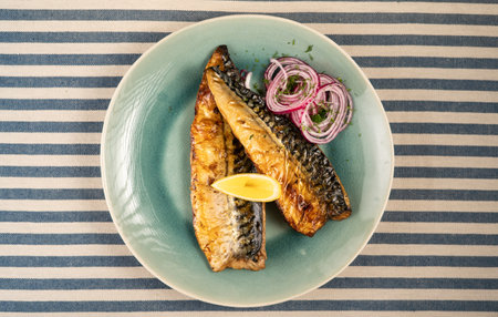 Grilled mackerel served on a plate with lemon and onion ringsの写真素材