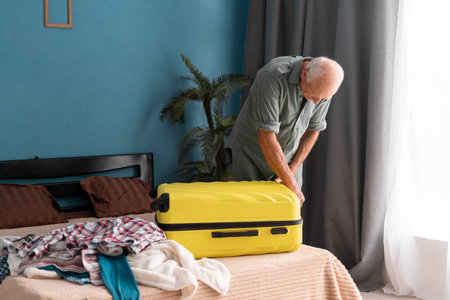 Traveling preparation. Senior man closing his suitcase preparing for vacation trip. Elderly man with luggage on the bed.の写真素材