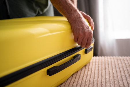Close-up of senior male hands packing and locking bag for holidays trip. Latino man preparing travel suitcase. Close-up of hands and zipper.の写真素材