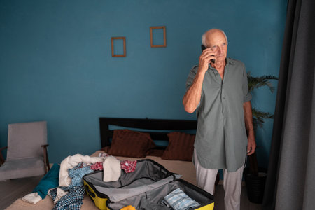 Retired man booking travel and packing suitcase at home for tripの写真素材