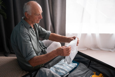 Travel concept. Retirement man preparing packing luggage bag for summer vacation trip sitting on bed...