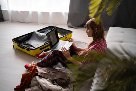 Senior traveler sitting on the floor with suitcases at home booking tickets online using laptop. Elderly woman preparing for holiday trip. Vacationの写真素材