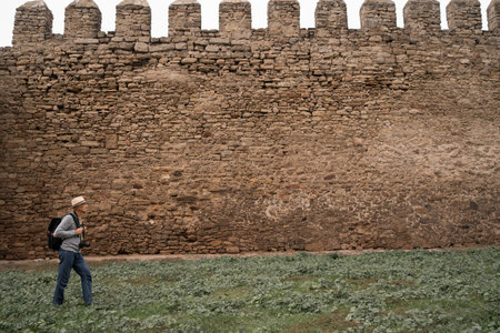 Old man visiting ancient fortress walks along stone wall with space for text. Tourism, travel and sightseeingの写真素材