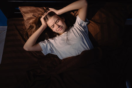 Waking up with a headache. Teen girl cant asleep restless on bed, having bad sleep troubles with headacheの写真素材