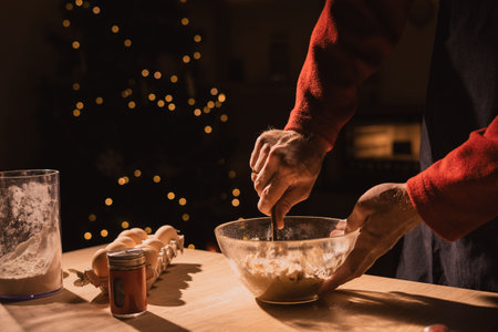 Close-up man in apron making dough for christmas gingerbread cookies while cooking in decorated kitchen, low angleの写真素材