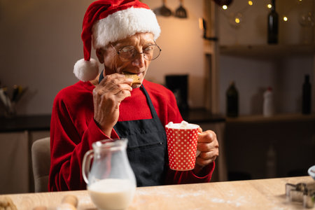 Caucasian retired man wearing Santa hat drink hot cocoa in cozy kitchen setting. Festive atmosphere with Christmas decorの写真素材