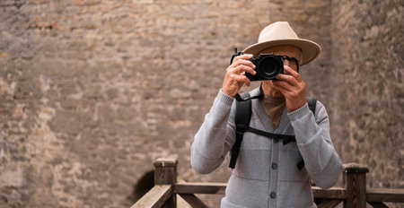Retiree man photographer with a camera takes pictures outdoors in old fortress. Elderly male photographer enjoys the process of shooting. travel to Europe countries. travel and vacation.の写真素材