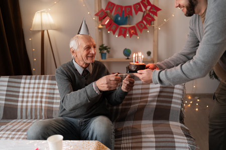 Adult son celebrating father birthday at home, presenting him with celebratory cake. Family celebration anniversary and fathers birthday.の写真素材
