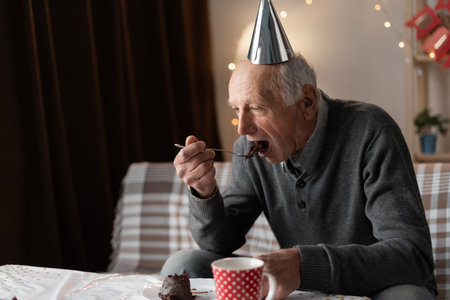 Lonely forgotten by children old man celebrating birthday alone eating holiday cake at home.の写真素材