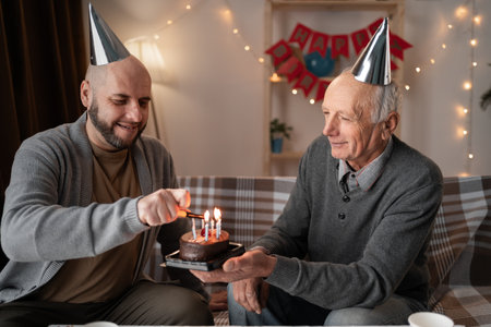 Elderly father and adult son lighting birthday cake candles togetherの写真素材