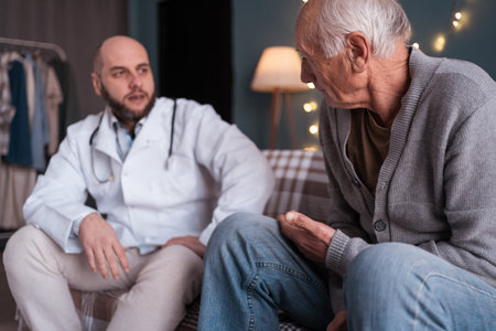 Concept of elderly people home care. Male professional doctor consulting senior patient at home visit. Man physician providing medical assistance for senior man while talking with himの写真素材