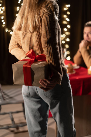 woman surprises a man with a gift standing in cozy living room while have romantic dinner, conveying love and celebrationの写真素材