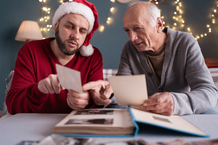 An elderly father looks at old photos with his adult son and shows pictures of him when he was young. The concept of family traditionsの写真素材