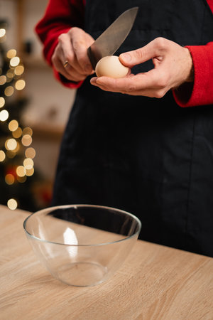 Man cracking egg with knife standing in kitchen preparing dough for Christmas baking, baking cookiesの写真素材