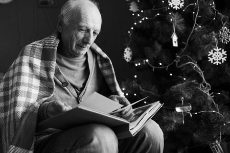 Retired man looking at photo album sitting in armchair grieving for dead wife on christmas eve....
