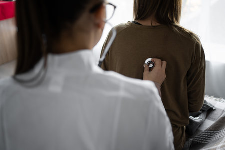 Female doctor using stethoscope while examining senior woman at home