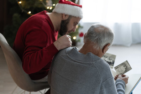 Elderly father and his adult son looking at old photos while spending time together sitting in the living room at homeの写真素材