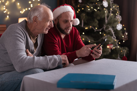 Two men family old father and adult son having fun enjoying using smartphone watching social media video on Christmas using mobile apps at homeの写真素材