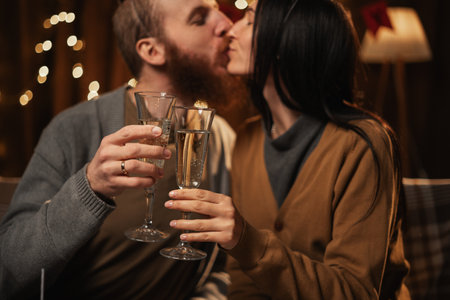 Happy young couple in love holding glasses, drinking champagne, celebrating Birthday at home together, having romantic dinner, bonding.の写真素材