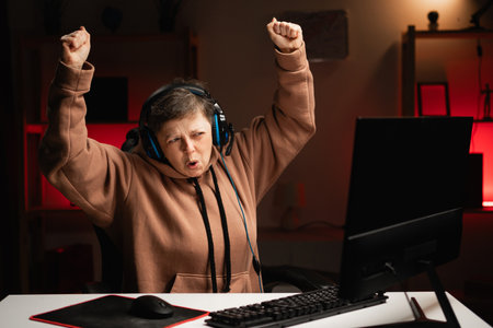 Successful female gamer winning online video game on computer. Lady wearing hoodie and headphones playing PvP tournament with other players at homeの写真素材