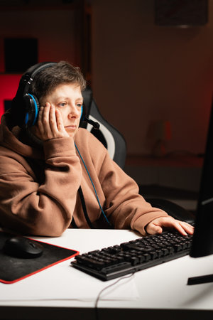 Tired bored middle aged female gamer dressed in hoodie playing online video games at home.の写真素材