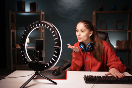 woman gamer streamer live streaming a video for her followers on social media while using smartphone and ring lamp at night, showing air kiss with love gesture.の写真素材