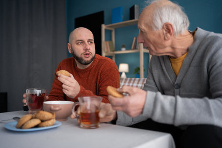 Family Togetherness concept. Senior father with adult son sitting and drinking in the living room at home.の写真素材