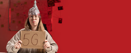 Female conspiracy theorist in protective foil cap and glasses debunks myths holding poster 5G. Conspiracy theory concept. Banner.の写真素材