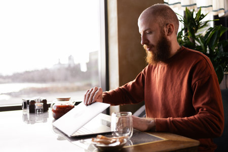 Remote work, freelance. stylish bearded Caucasian man works sitting in a cafe. Opens his laptop.の写真素材