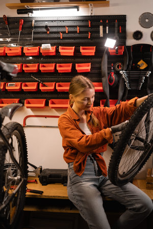 Caucasian young female mechanic worker repairing bicycle wheel while standing in bike workshop