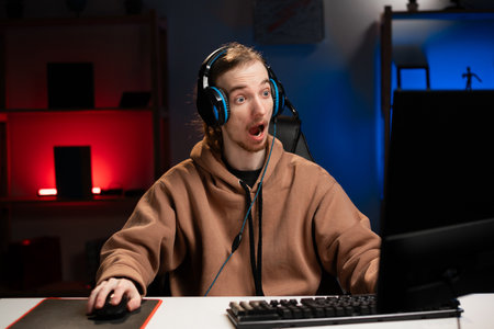 Amazed Shocked pro gamer with open mouth playing in online cyber sport game at night at homeの写真素材