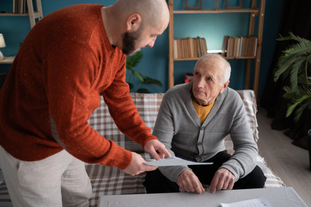 Loving adult son helping senior father paying bills and doing paperwork at home. Aid on retirement.の写真素材