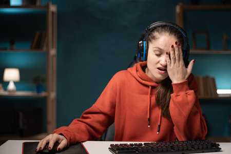 E-sport woman gamer play game at night at home. Young lady gaming player feel stress and negative emotion holding head suffer headache broadcast live streaming online game.の写真素材