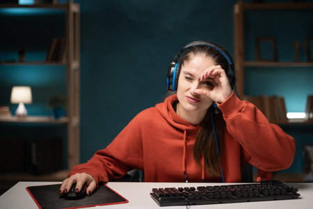 E-sport woman gamer play game at night at home. Young lady gaming player show okay sign make binoculars watch look, broadcast live streaming online game.の写真素材