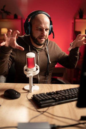 Bearded man playing online computer video game, broadcast streaming live at home, showing gesture tiger nails. Gamer lifestyle and online gamingの写真素材