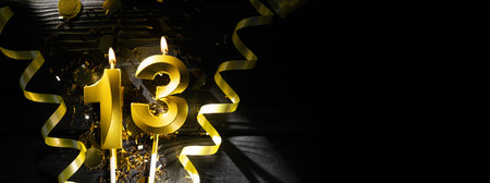 A golden candle in the shape of the number thirteen burns on a dark table in beams of light, surrounded by sparkling confetti and spiral ribbons, creating an authentic atmosphere.の写真素材