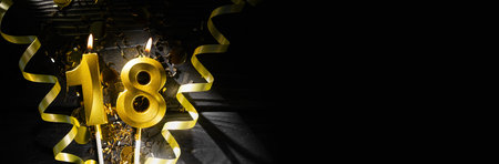 A golden candle in the shape of the number eighteen burns on a dark table in beams of light, surrounded by sparkling confetti and spiral ribbons, creating an authentic atmosphere.の写真素材