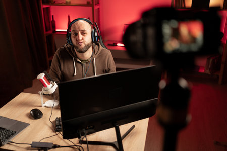 Gamer streamer playing online game on PC in dark room. Sitting in front of camera recording video with dissatisfied expression. e-Sport Games and Internet Championship.の写真素材