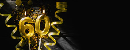Golden candles number sixty burning brightly, celebrating 60th birthday anniversary. Festive ribbons and confetti on black background, creating elegant celebratory banner.の写真素材