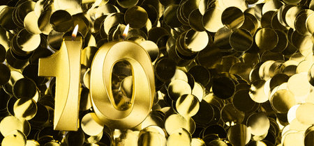Golden number ten candle on shiny yellow confetti background. Festive backdrop for tenth birthday, anniversary or celebration. Bright greeting card with space for text.の写真素材